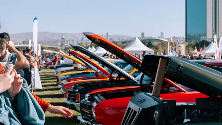 A line of vehicles with their hoods raised at an outdoor event