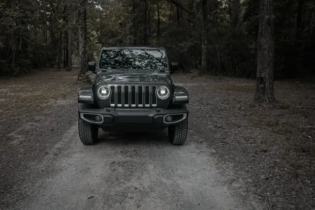 Front view of a dark Jeep Wrangler parked on a forest trail at dusk
