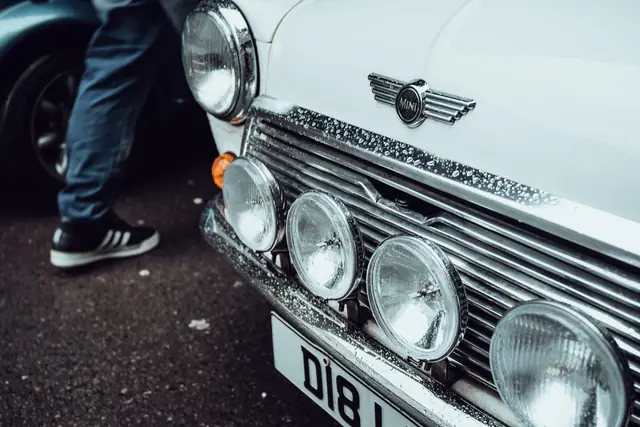Front detail of a white classic Mini with round headlamps and auxiliary driving lamps