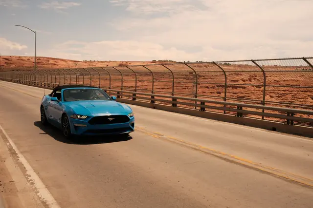 A blue Ford Mustang convertible driving on a road across a bridge